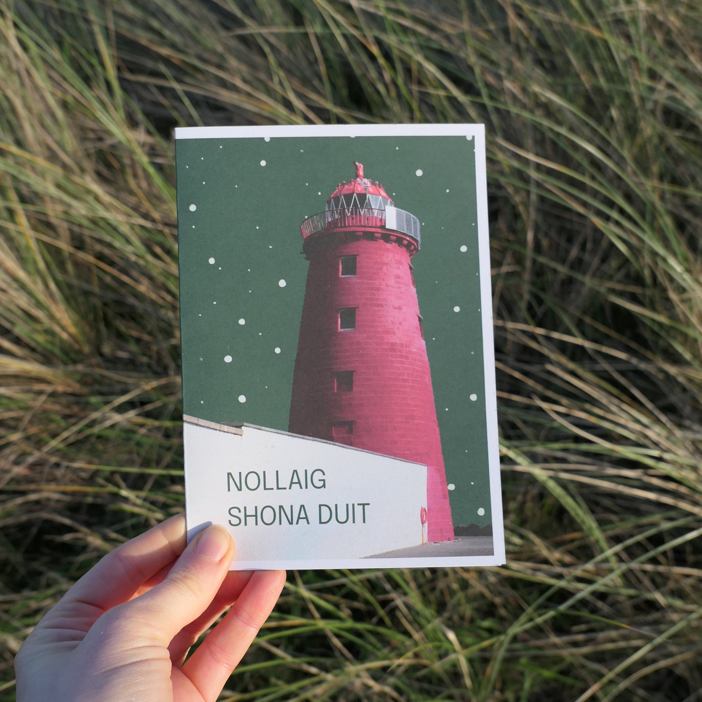 Hand holding a card with a lighthouse design of Dublin against a grassy background